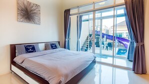 A modern hotel room with a large bed, a view of a pool and outdoor area, and a glass door leading to the balcony. - Baan Chom Chan Pool Villa (Hua Hin)