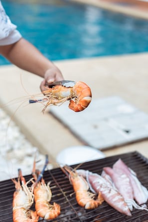 A person grilling shrimp and fish by a poolside.