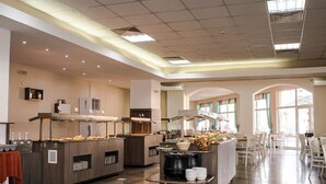 Una amplia cafetería con varias estaciones de servicio, una zona de buffet central y un área de comedor con mesas y sillas.