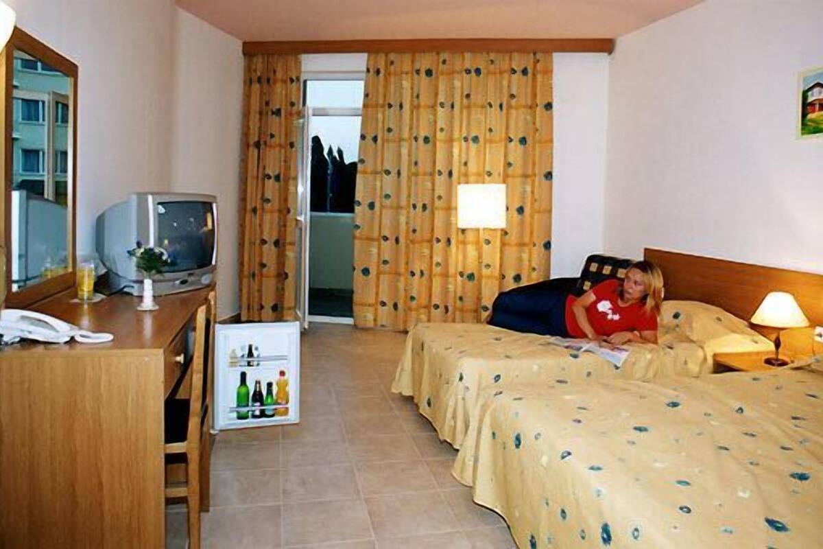 A hotel room with a bed, a desk with a telephone, a television, and a small refrigerator.