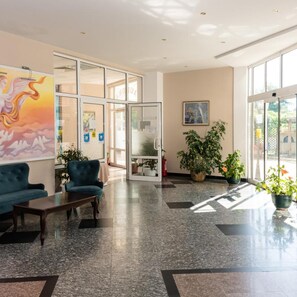 A lobby with a blue sofa, a wooden coffee table, a large painting, potted plants, and a glass door leading to another room. - Hotel Aurora - All Inclusive (Varna)