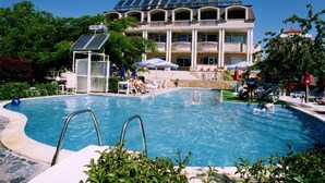 Una piscina con un edificio iluminado por el sol al fondo, rodeada de follaje.