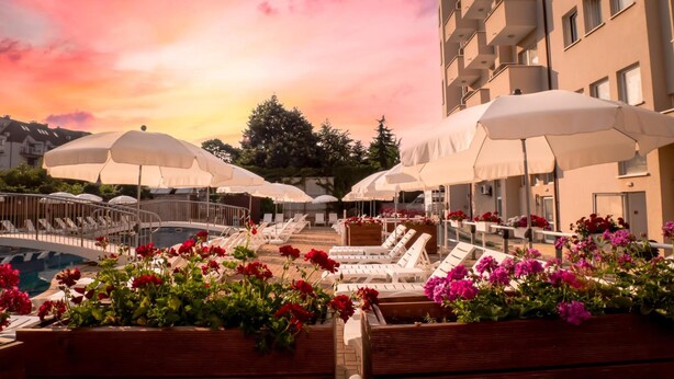 Zona junto a la piscina con tumbonas y sombrillas, rodeada de macizos de flores.