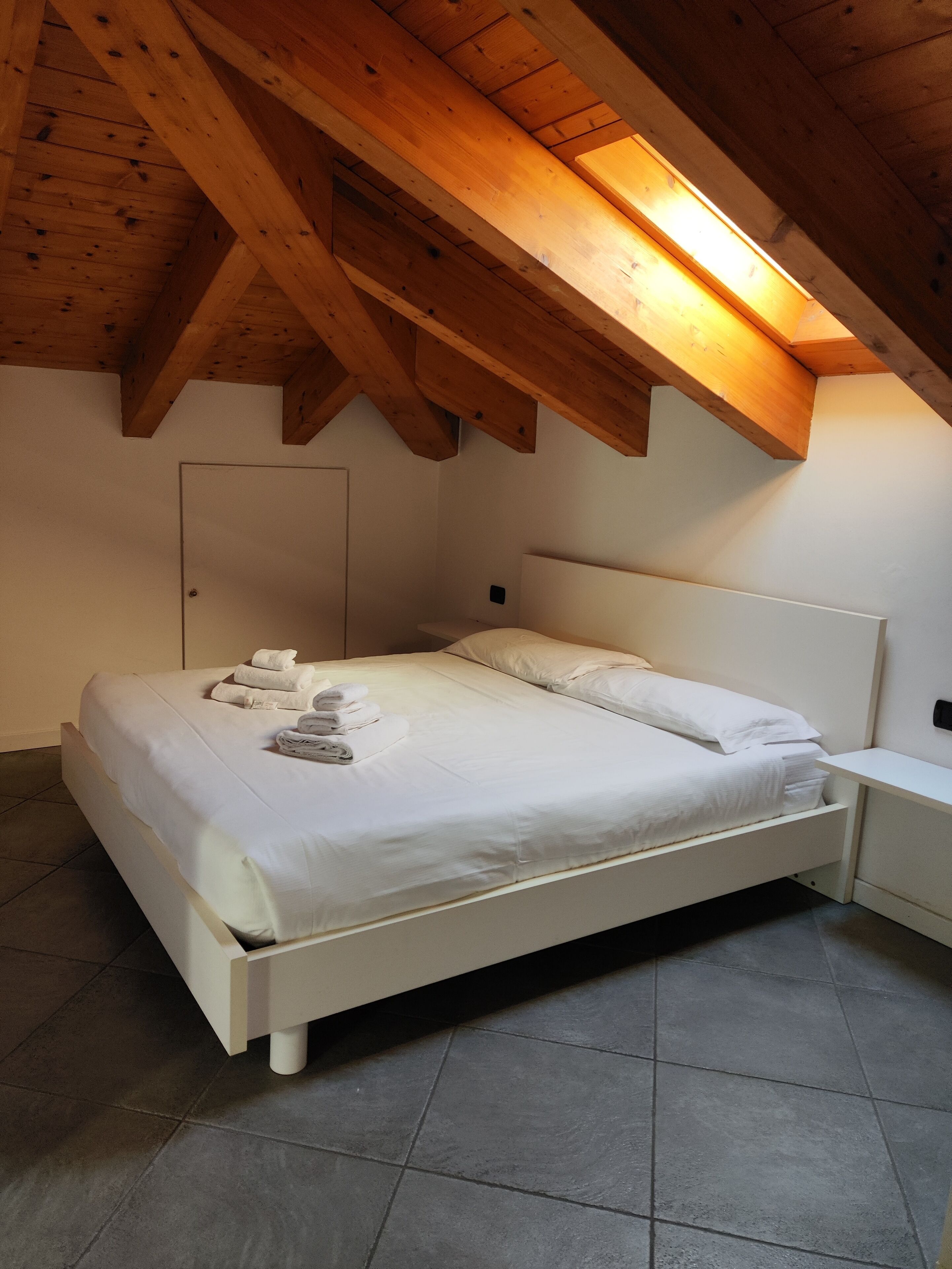 A bedroom with a white bed, neatly made with towels, a white nightstand, and a wooden ceiling.