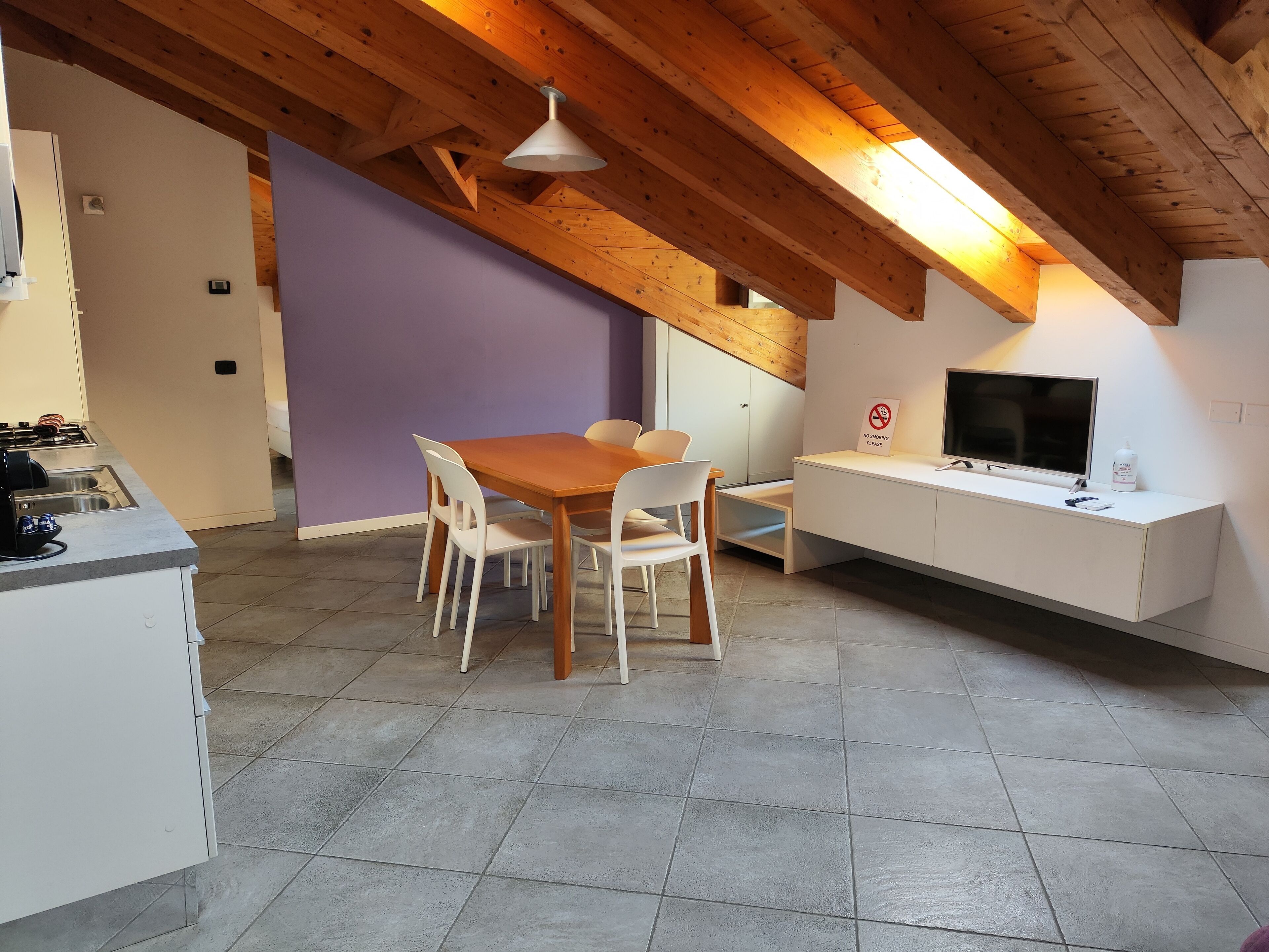 Una cocina moderna con comedor, vigas de techo de madera y un televisor sobre un mueble blanco.