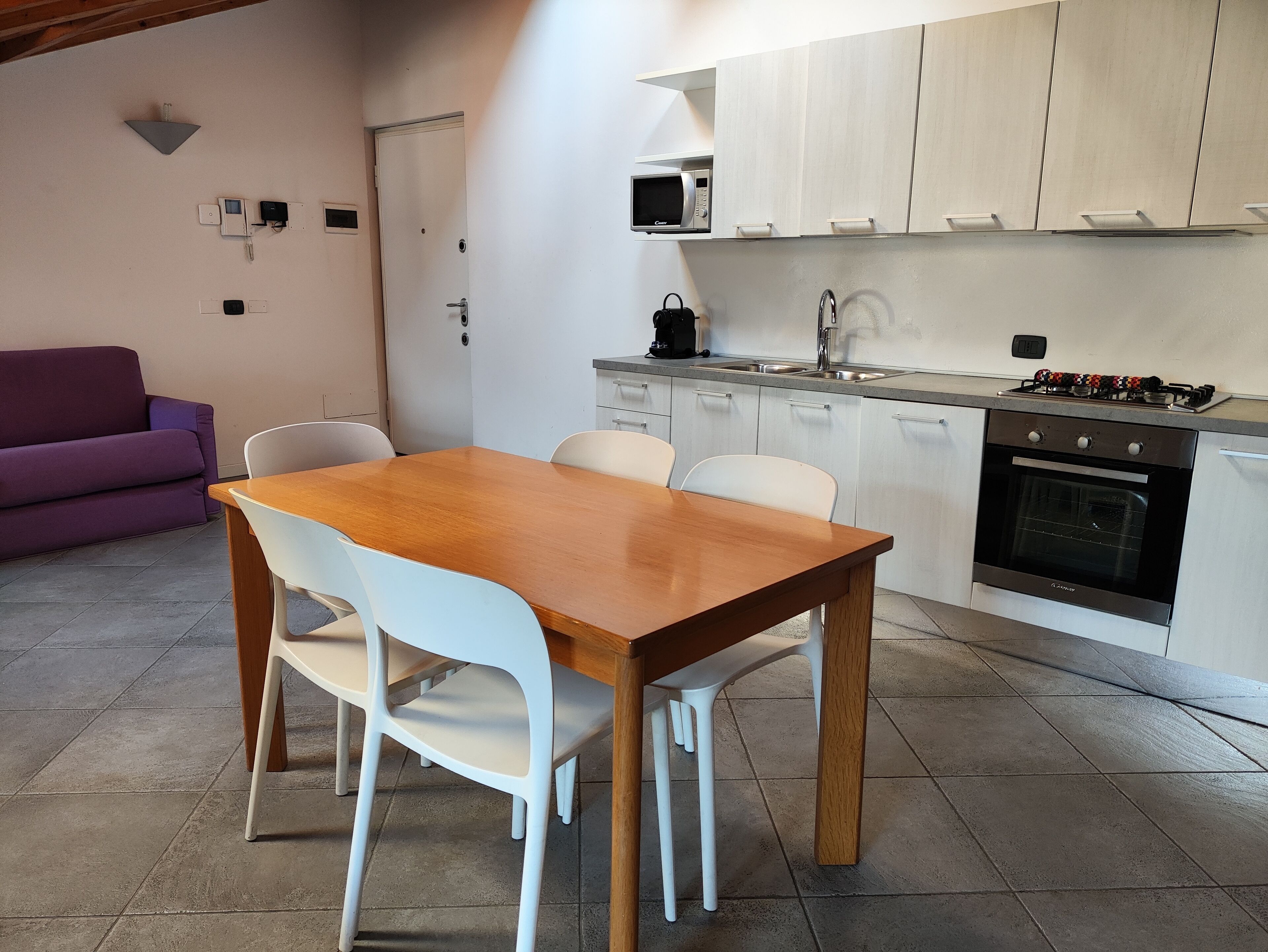 Una cocina compacta con una mesa de comedor de madera y sillas blancas, horno empotrado y microondas sobre el fregadero.