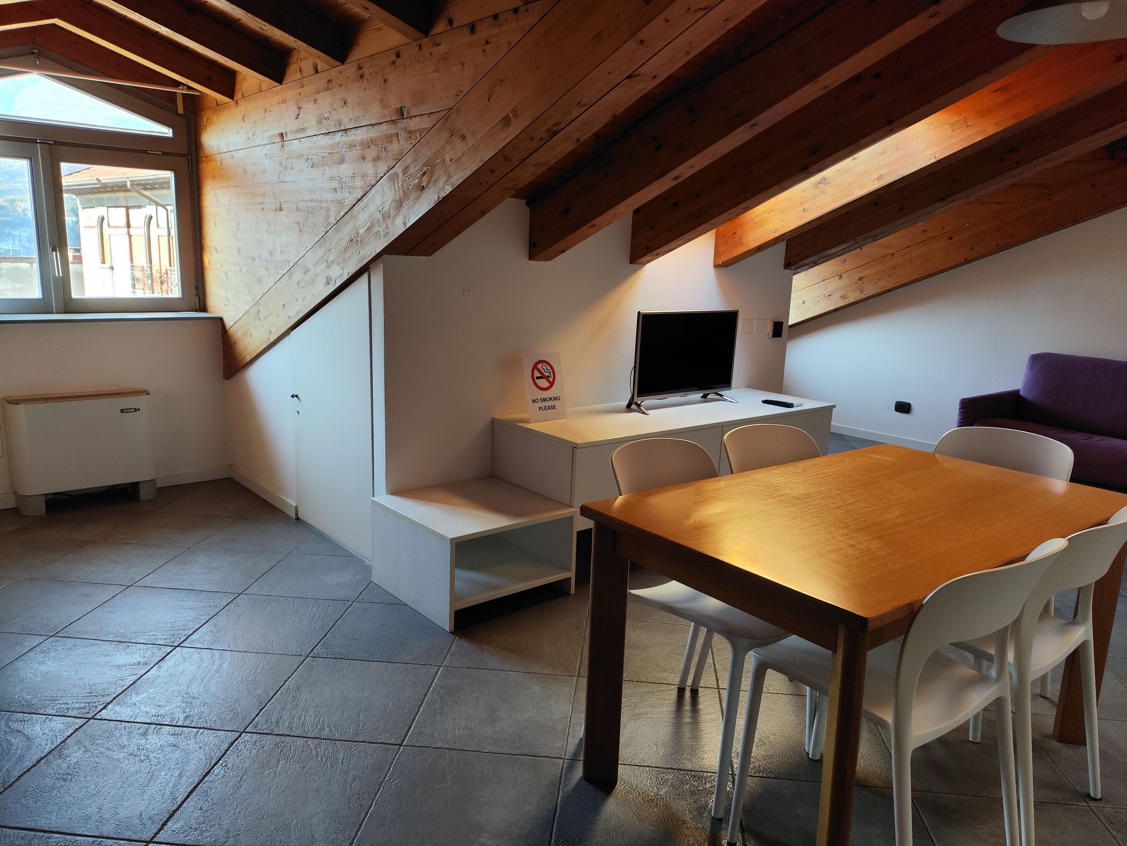 Un ambiente compatto con soffitto in legno, un tavolo da pranzo con sedie, un angolo cottura, una TV e un divano.