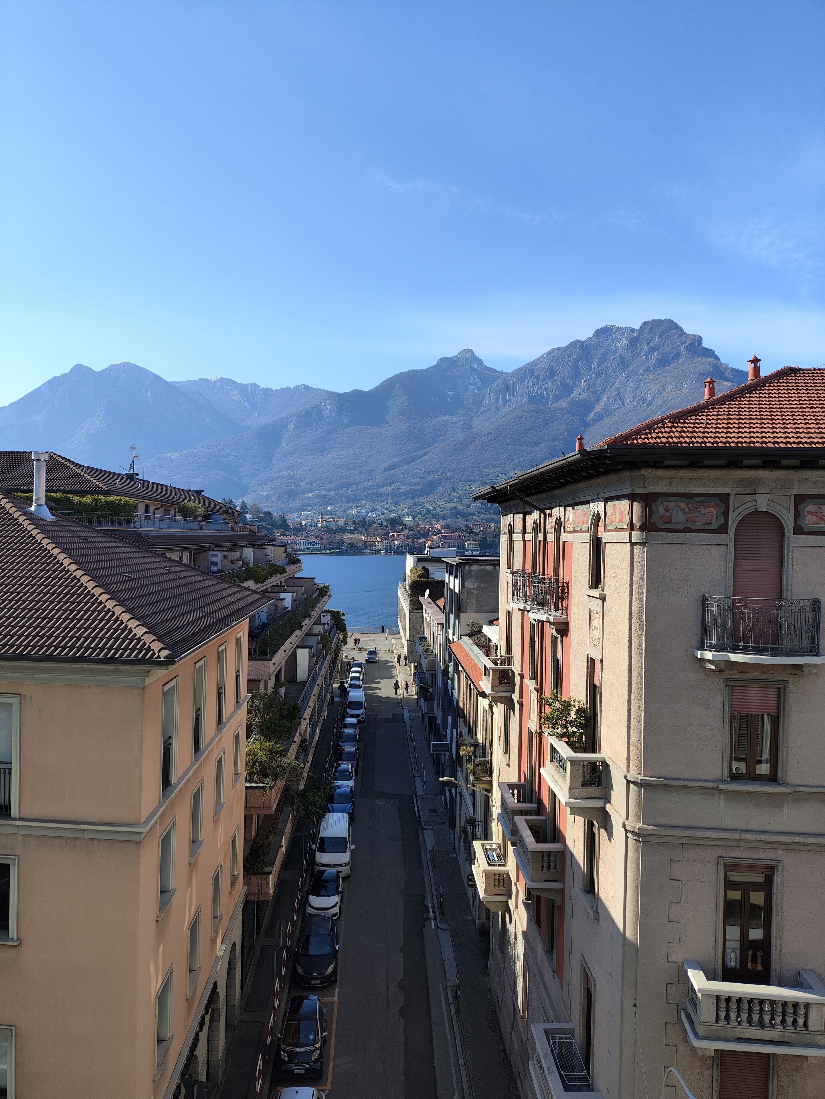 Una calle flanqueada por edificios, cielo despejado y montañas al fondo.