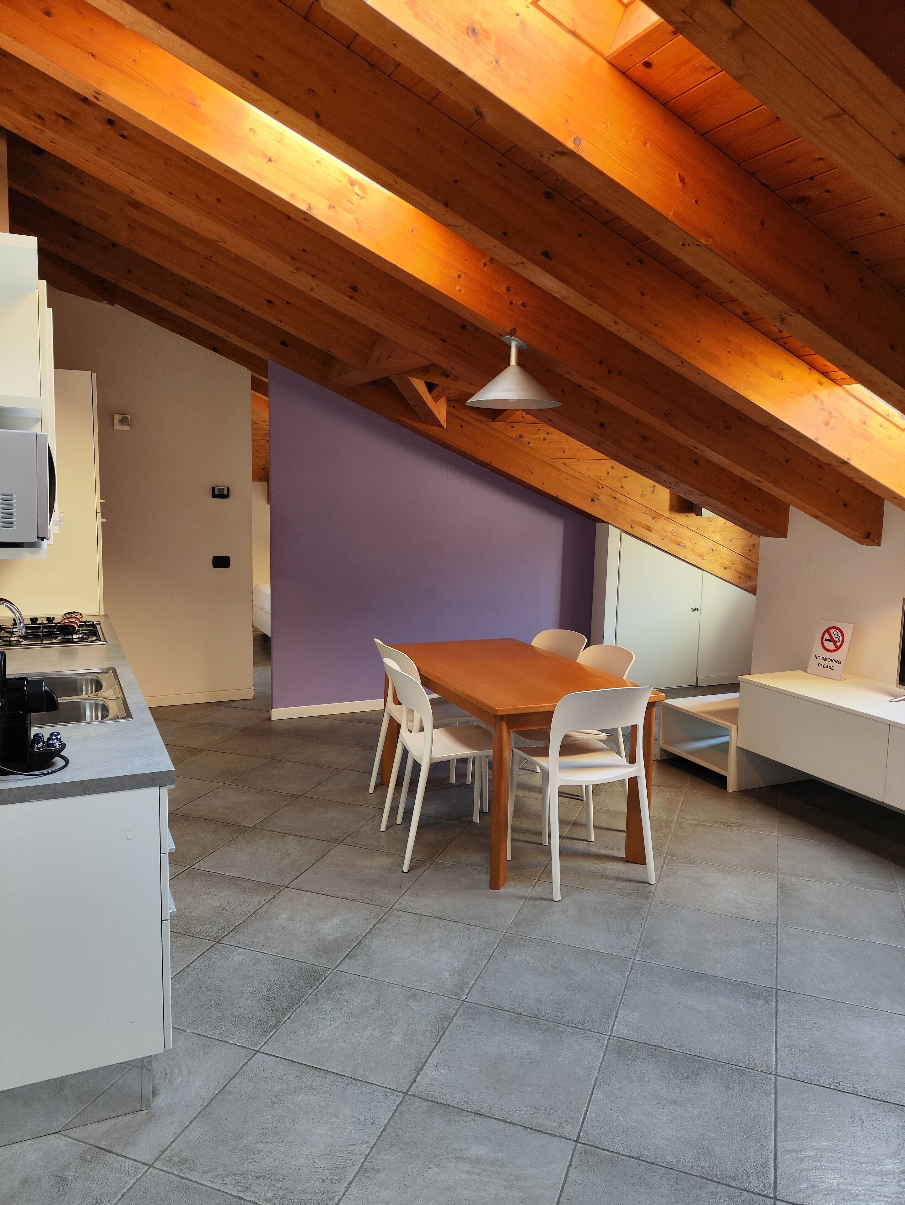 A modern kitchen with a dining area, wooden beams, and a purple accent wall.