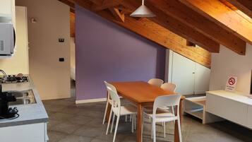 A modern kitchen with a dining area, wooden beams, and a purple accent wall.