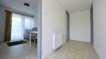 Een modern appartement met een houten vloer, een radiator, een raam met dunne gordijnen en een groen vloerkleed.