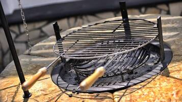 Un barbecue extérieur de forme ronde, doté d’une grille en métal et d’un foyer à charbon, installé sur une surface en pierre.
