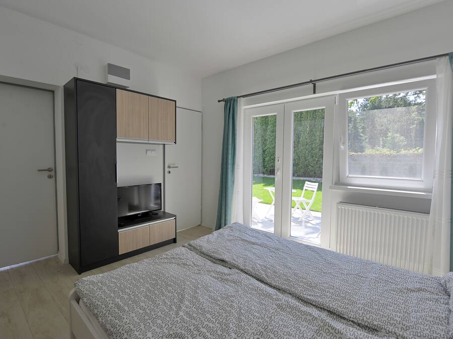 Een slaapkamer met een bed, een televisie, een kledingkast en een schuifdeur naar een balkon.