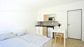 A compact bedroom with a bed, a small kitchenette, and a door.