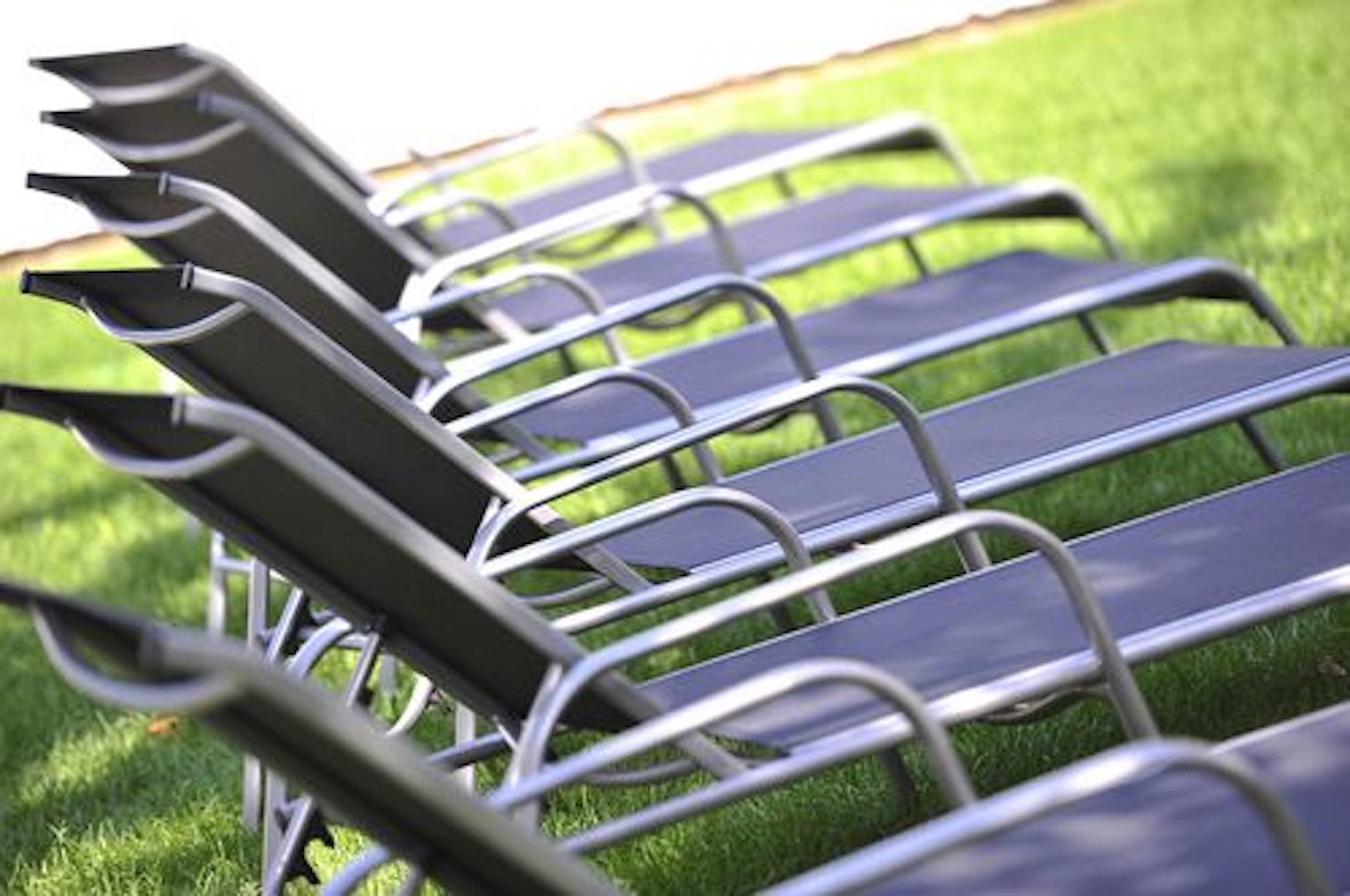 A row of metal lounge chairs with metal frames and dark cushions, arranged on a grassy area.