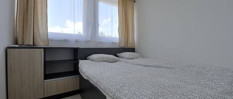 Un dormitorio con una cama, dos ventanas con cortinas, un estante empotrado y suelo de madera.