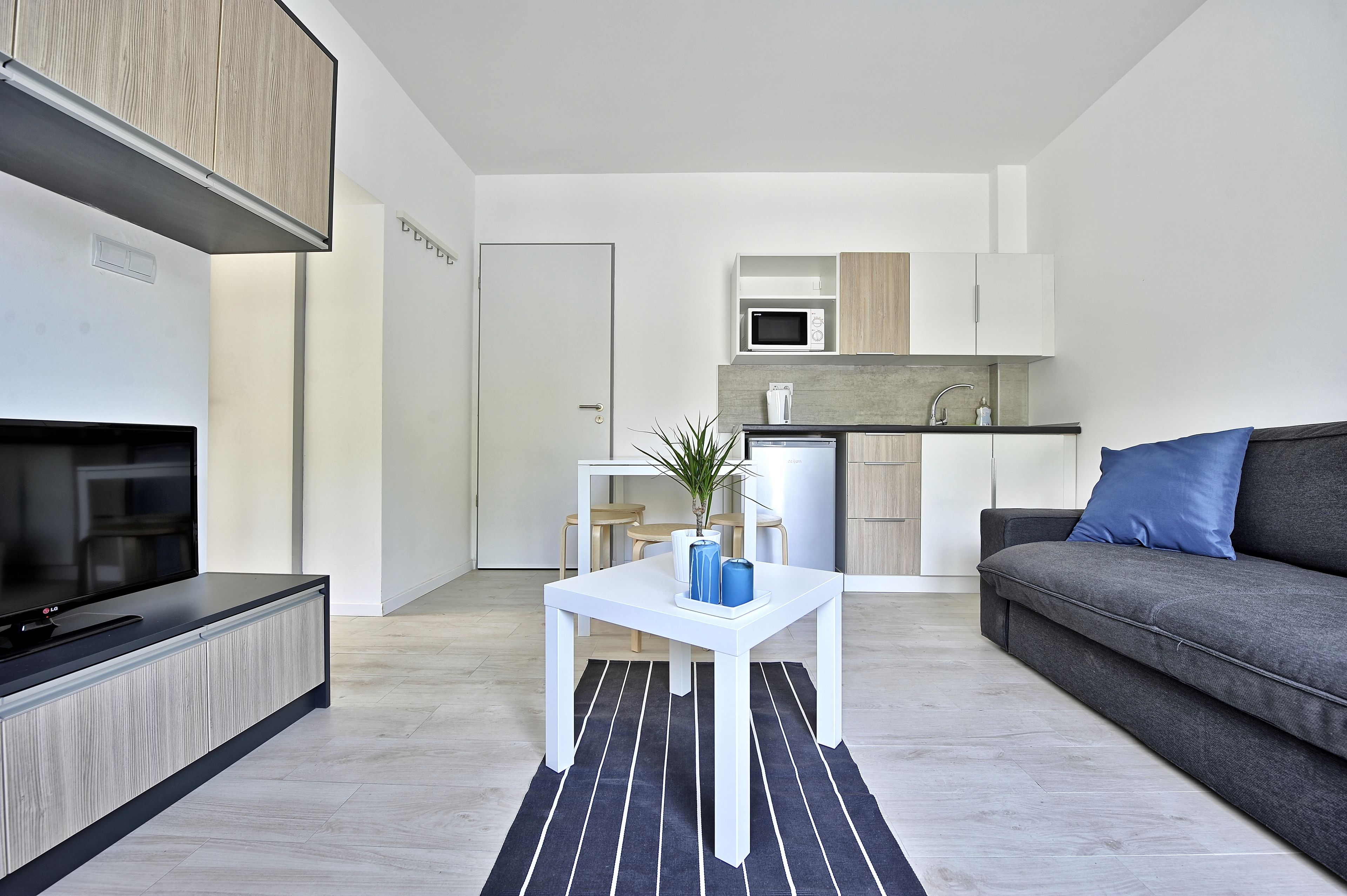 Una sala de estar moderna con un televisor de pantalla plana, un sofá gris, una mesa de centro blanca y un tapete a rayas negras y blancas.