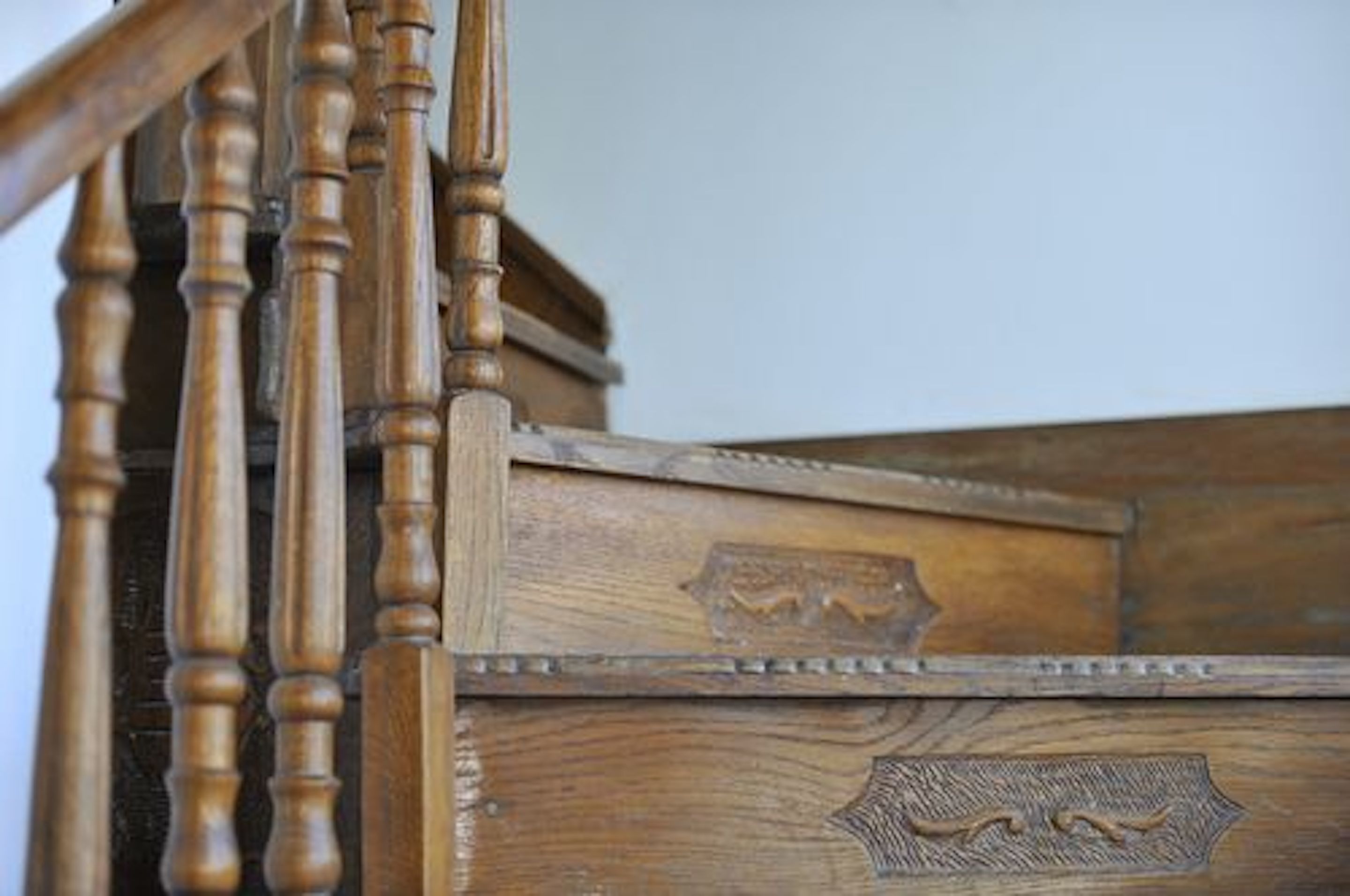 Una escalera de madera con detalles tallados y un cofre de madera al pie.