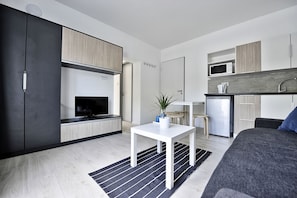 Un espacio habitable moderno y compacto con kitchenette, comedor y televisor.