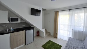 Una cuina moderna amb microones, nevera petita i un rentapeus. S'hi observa una escala que condueix a un dormitori amb llit i finestra amb cortines translúcides.