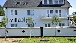 Una vila de dues plantes amb un balcó, un cartell amb el nom i una petita zona de jardí.