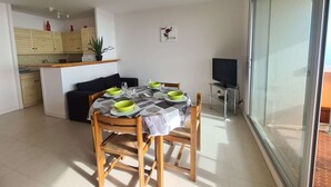 A dining area with a table set for four, a black sofa, and a kitchen in the background. - Seafront 3-Room Apartment with Balcony, Pool, and Private Parking - Sleeps 4 (Saint-Jean-de-Monts)