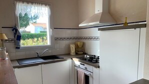 A compact kitchen with white cabinets, a gas stove, a sink, and a window with a view of greenery. - House near pond, enclosed garden, 2 bedrooms (Bretignolles-sur-Mer)