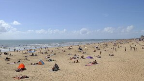 Une plage bondée, avec des tentes et des gens qui prennent des bains de soleil.