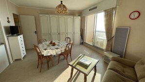 Un coin repas avec une table et des chaises, un canapé, un téléviseur posé sur un meuble et une horloge au mur.