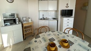 Une cuisine compacte équipée d’un four à micro-ondes, d’un grille-pain et d’un évier. On y trouve une table à manger avec deux chaises et un téléviseur posé sur un meuble.