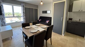 A compact kitchen with a dining area, a small sofa, and a window with curtains. - Beautiful apartment with parking near the beach, 2 rooms, 4 people (Saint-Jean-de-Monts)