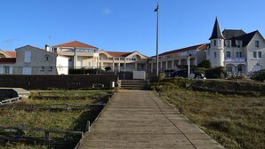 A wooden boardwalk leading to a coastal building with multiple windows and a flagpole. - 2-room apt closed terrace near beach (Saint-Hilaire-de-Riez)