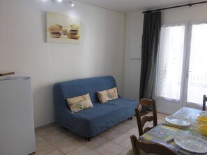 Un espace de vie compact comprenant un canapé bleu, une table à manger mise avec des assiettes et des verres, et un réfrigérateur.