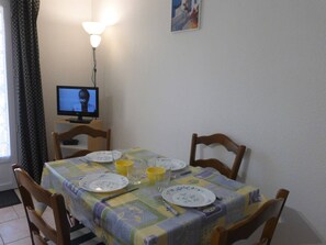 Un coin repas avec une table dressée pour quatre personnes, un téléviseur posé sur un meuble et une lampe fixée au mur.