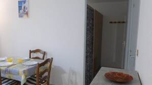 A dining area with a table set for two, chairs, a painting on the wall, and a door leading to another room. - 2-room apt closed terrace near beach (Saint-Hilaire-de-Riez)
