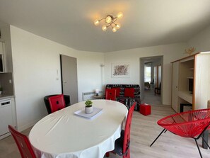 Uma área de refeições com uma mesa redonda, cadeiras vermelhas, um pequeno vaso de planta e um lustre.