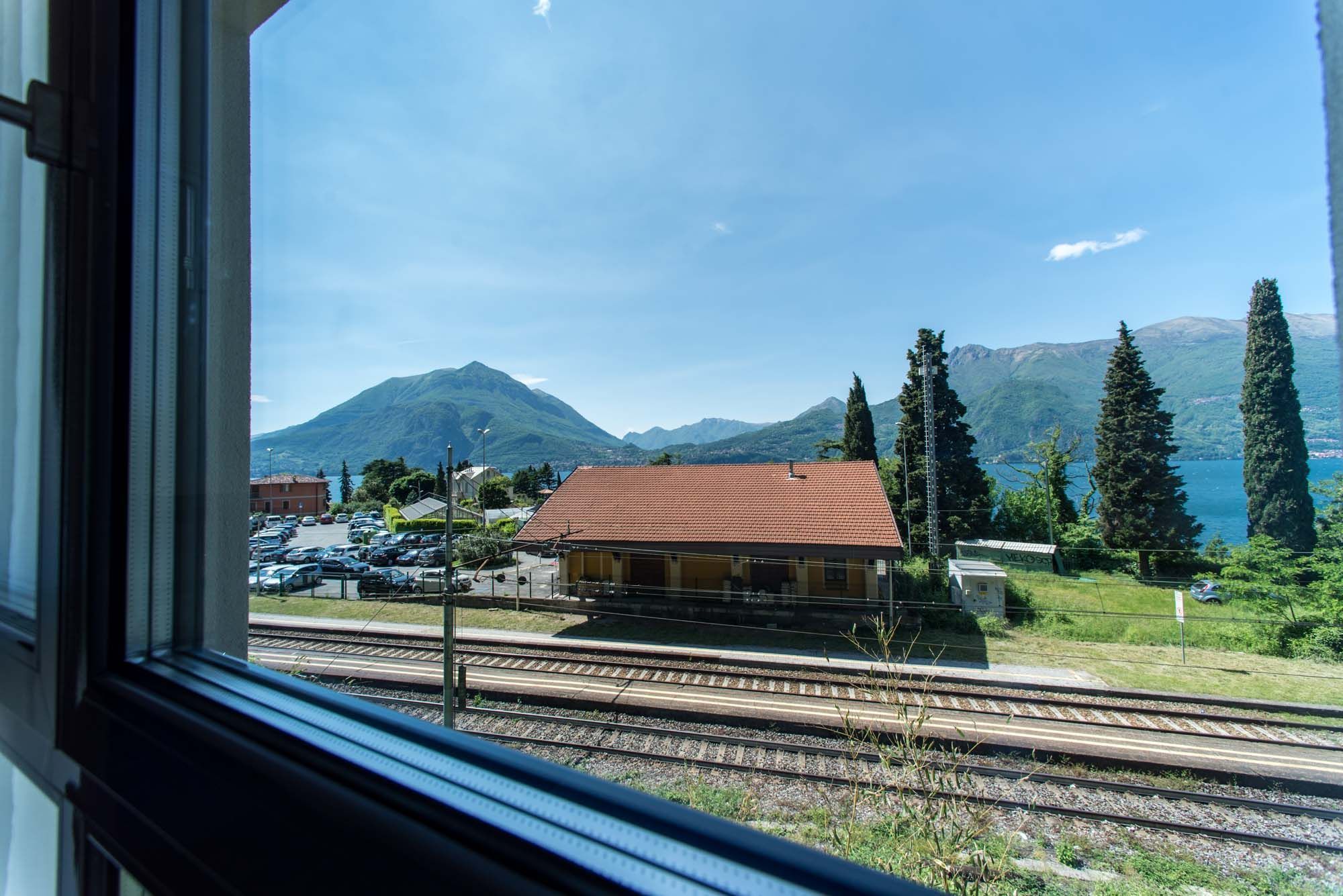 A view of a train station with tracks, a building with a red roof, and mountains in the background.