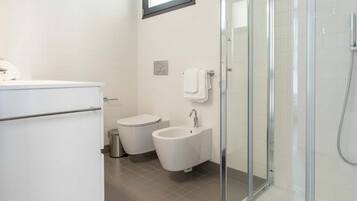 Een moderne badkamer met een douchecabine van glas, toilet, bidet en wastafel.