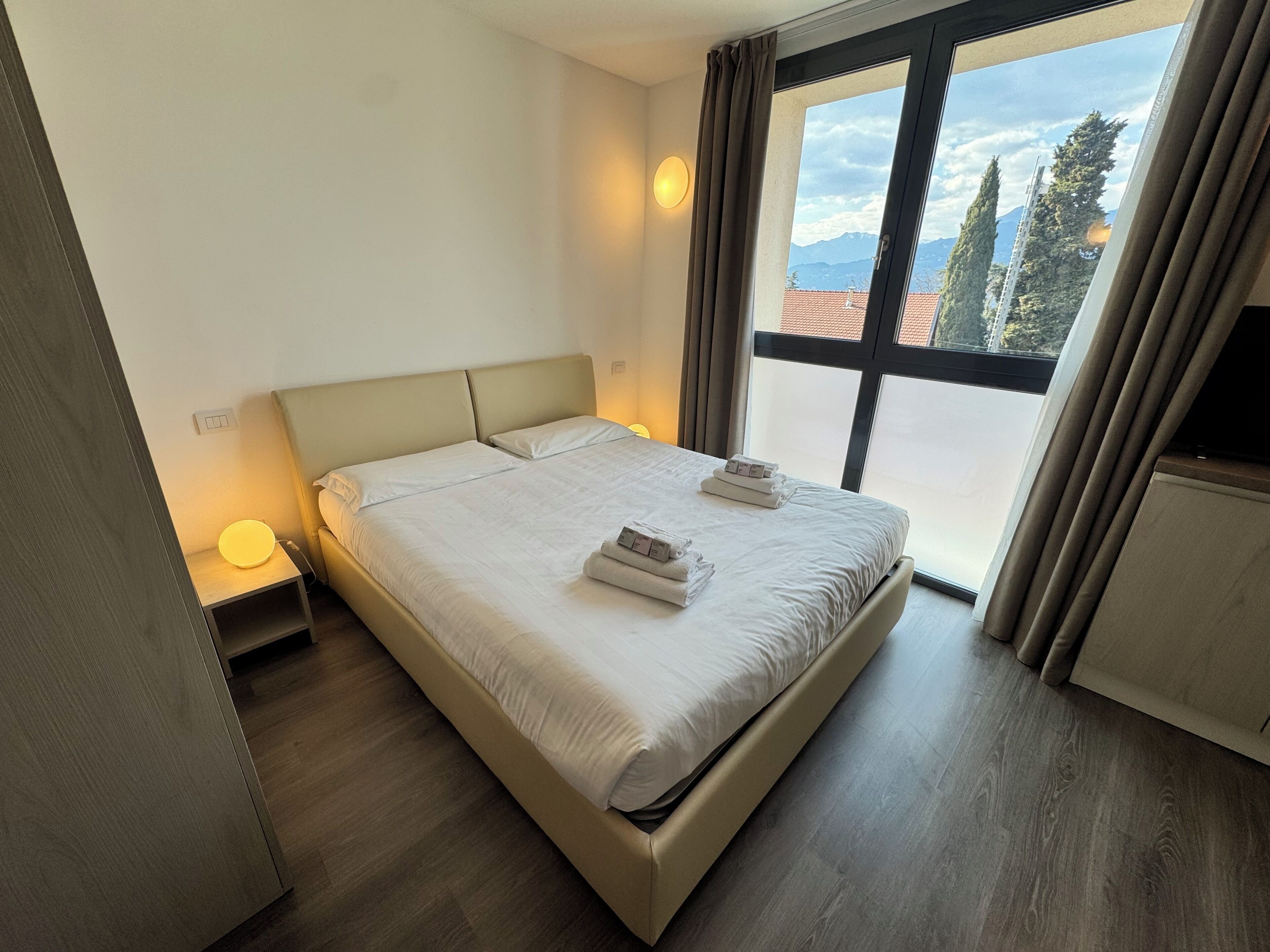 Ein ordentlich bezogenes Bett mit Kissen, einer Nachttischlampe und Bergblick durch ein Fenster.