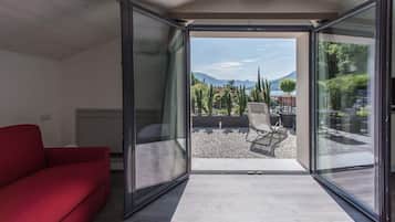 Un interior moderno con un sofá rojo, una puerta de vidrio que da a una terraza exterior con vistas a montañas y árboles.