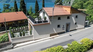 A two-story building with a balcony, a stone wall, and a view of a lake and mountains. - Residenza Decimina (Perledo)