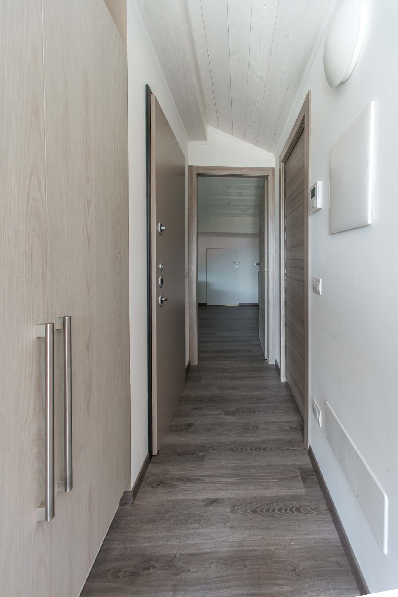 A hallway with wooden flooring, a door with a frosted glass panel, and a wall-mounted light fixture.