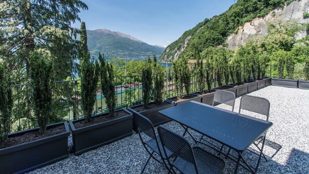A terrace with a table and chairs, surrounded by greenery and a view of a lake and mountains. - Residenza Decimina (Perledo)