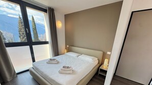 A modern hotel room with a large bed, two bedside lamps, and a view of mountains through a large window. - Residenza Decimina (Perledo)