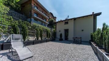 A courtyard with a lounge chair, a small outdoor table, and a building with balconies and a stone wall.