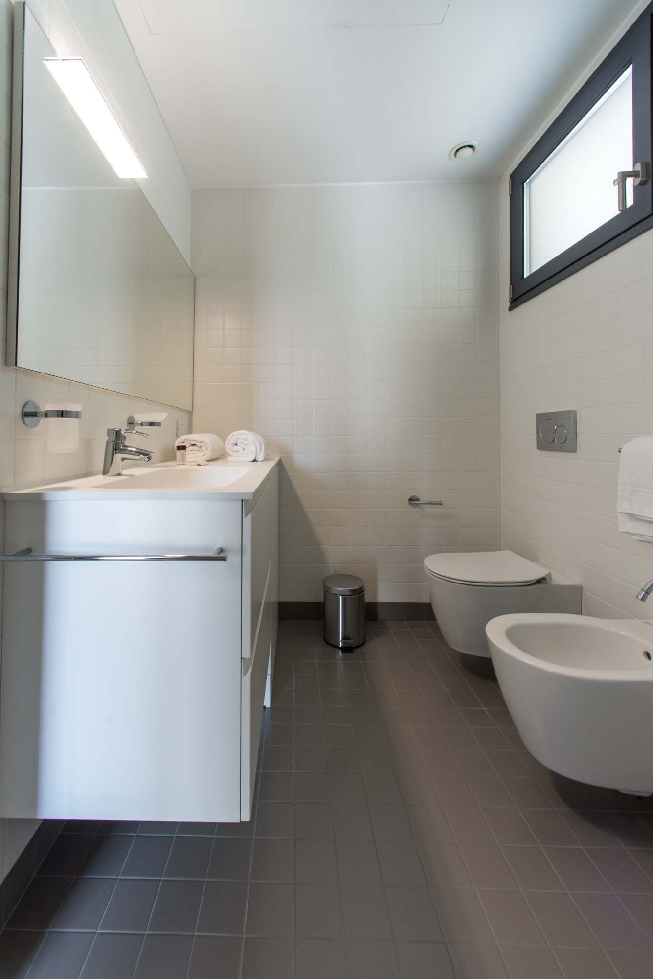 Een moderne badkamer met een wastafel, spiegel, toilet en bidet.