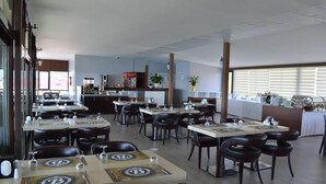 A restaurant with multiple tables and chairs, a kitchen area, and large windows with blinds. - Bal Otel (Tirebolu)