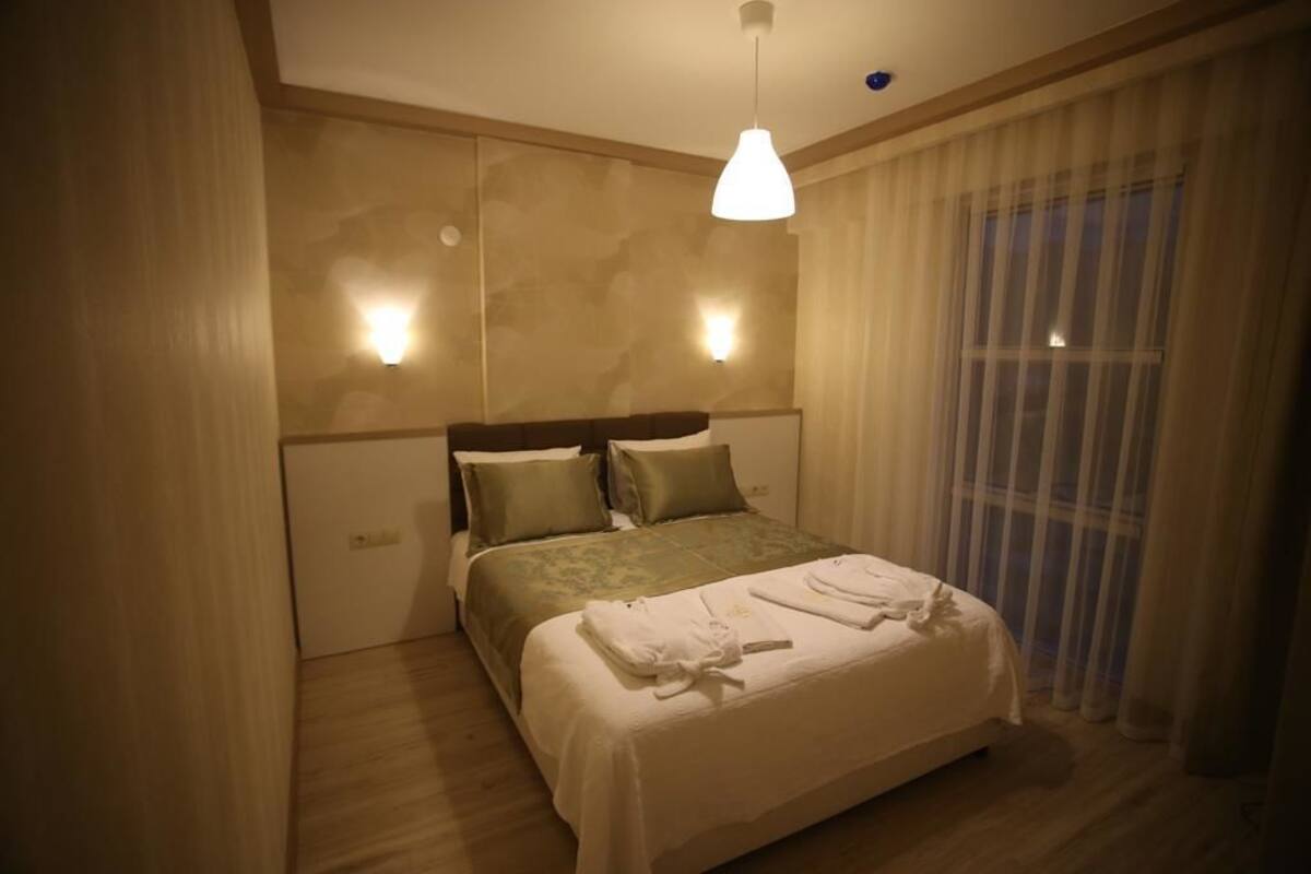 A hotel room with a large bed, two bedside tables, a hanging light fixture, and sheer curtains.