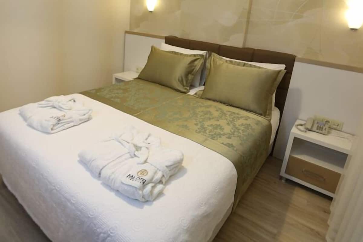 A neatly made bed with two towels, a bedside table with a phone, and a wall-mounted light.