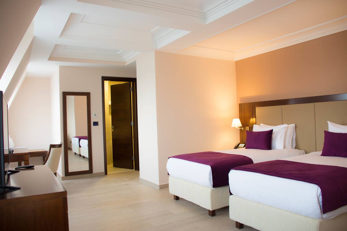 Habitación de hotel con dos camas, un escritorio, una silla y un espejo.